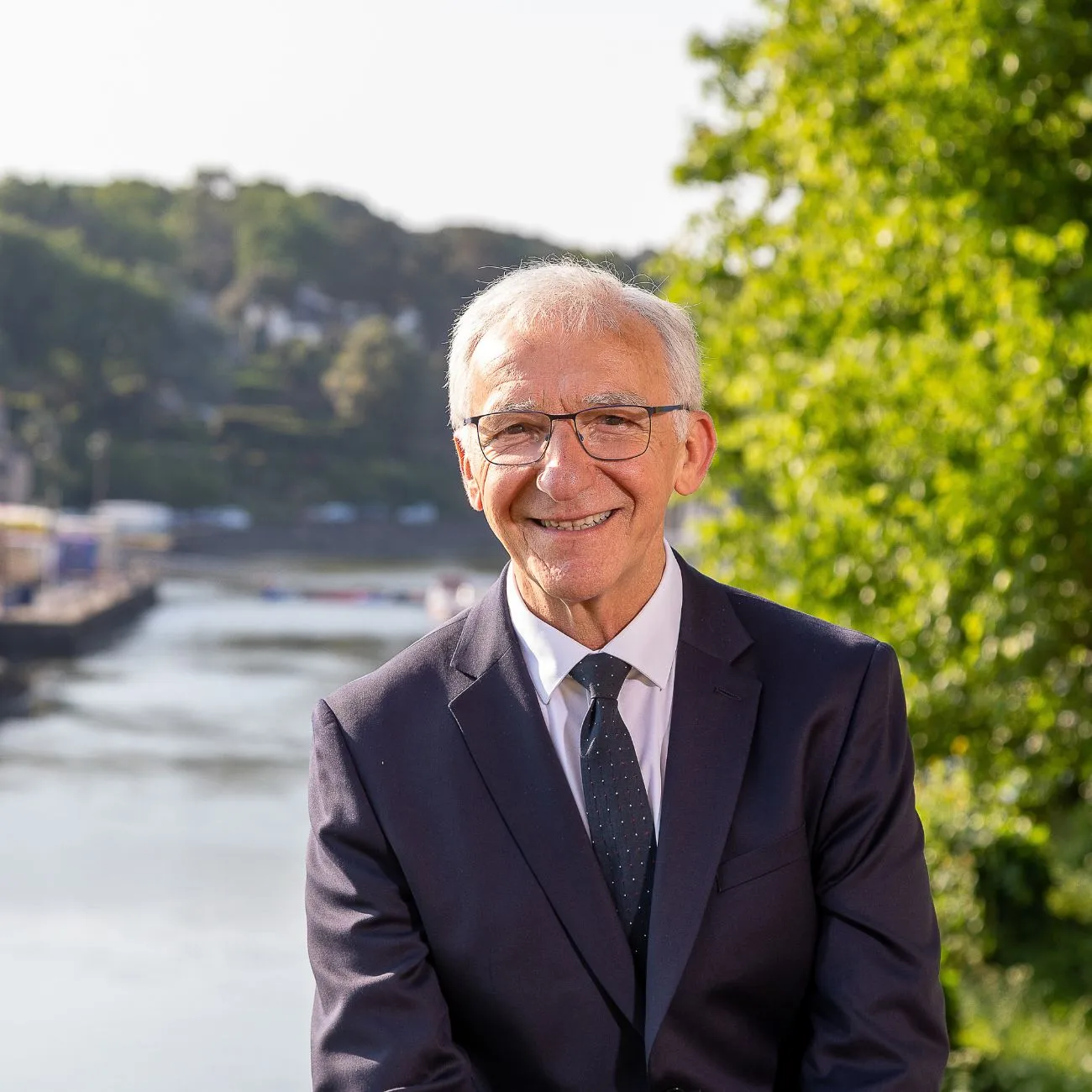 Portrait du candidat de la campagne Auray Cap 2026, en costume, souriant en extérieur à Auray avec la rivière en arrière-plan
